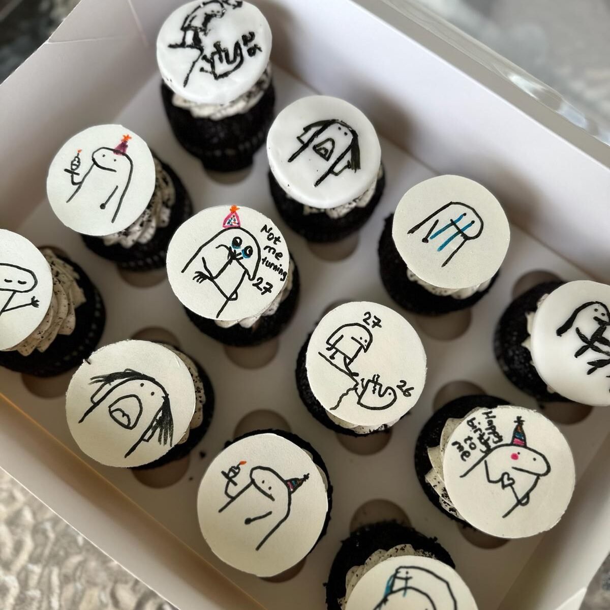 Et utvalg fargerike cupcakes utstilt på pastellfargede fat. Cupcakene er pyntet med rosa og hvit krem, dryss i ulike farger og sjokoladebiter. Noen har mørk sjokoladekakebunn, andre lys vaniljebunn.